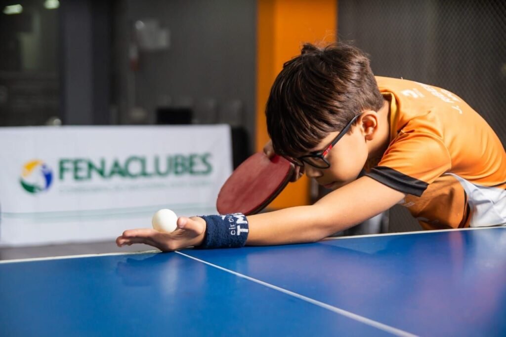 Jovem Menino de camisa laranja se preparando para jogar tênis de mesa