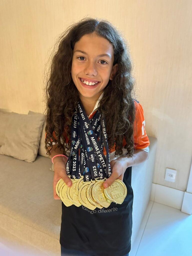 Menina segurando 8 medalhas de Ouro que conquistou ao vencer campeonatos de Natação, seu nome é Beatriz Oliveira