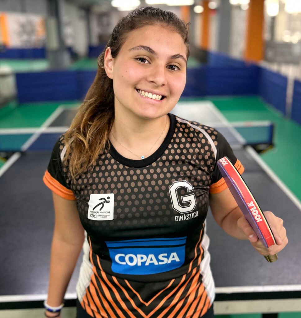 Menina de uniforme do ginástico, segurando uma raquete, a mesma é Jogadora de Tênis de Mesa