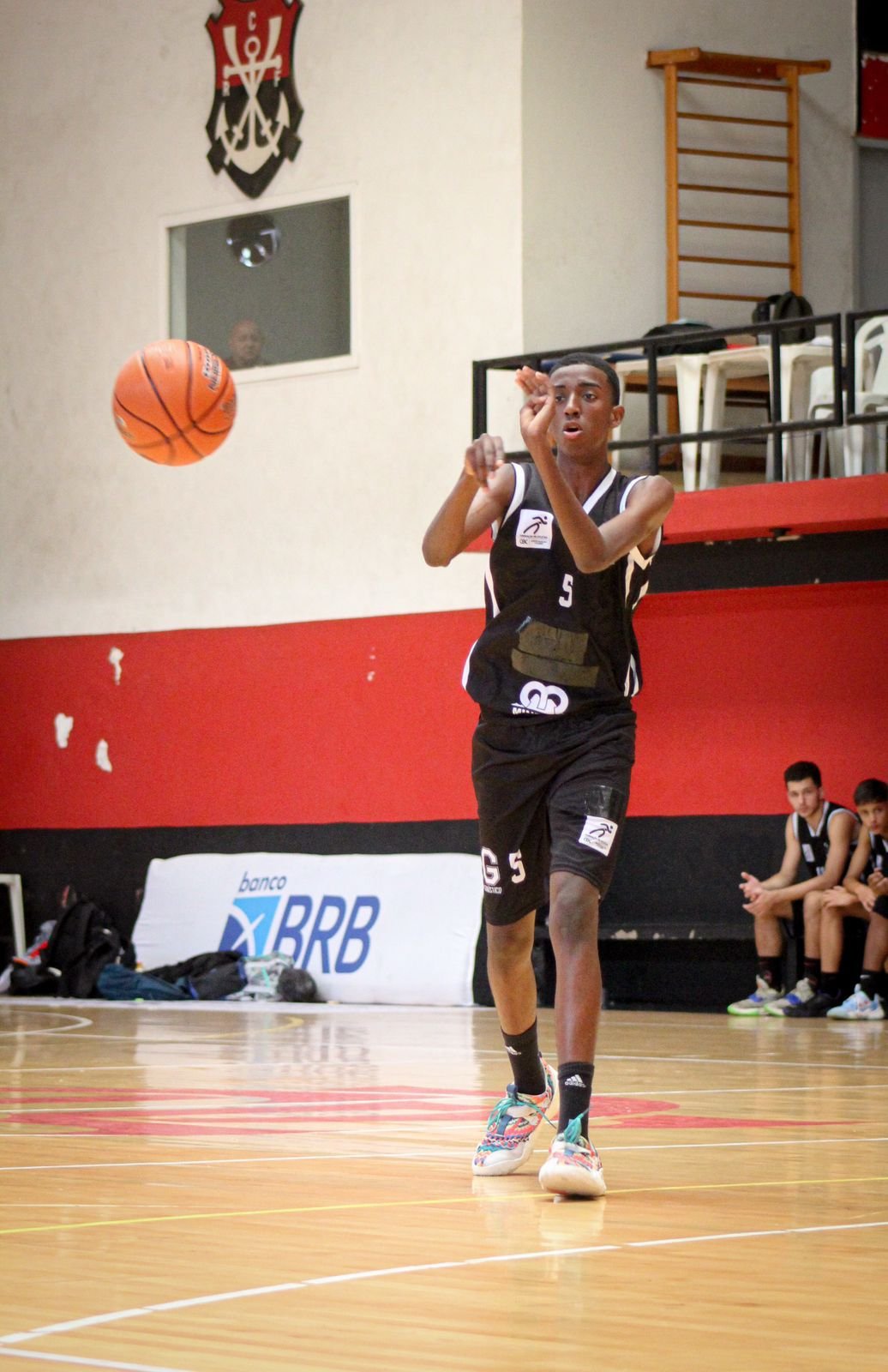 Jovem arremessando uma bola, ele está na Escola de Basquete