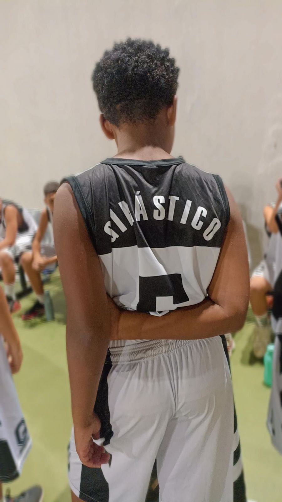 Foto de um jovem de costas atento a explicação, na Escola de Basquete