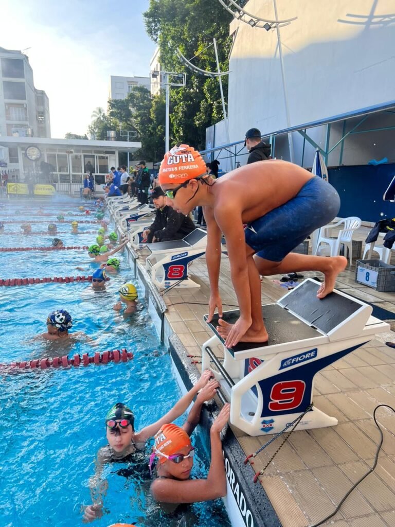 Jovem de shorts e toca de natação se preparando para nadar na piscina olímpica